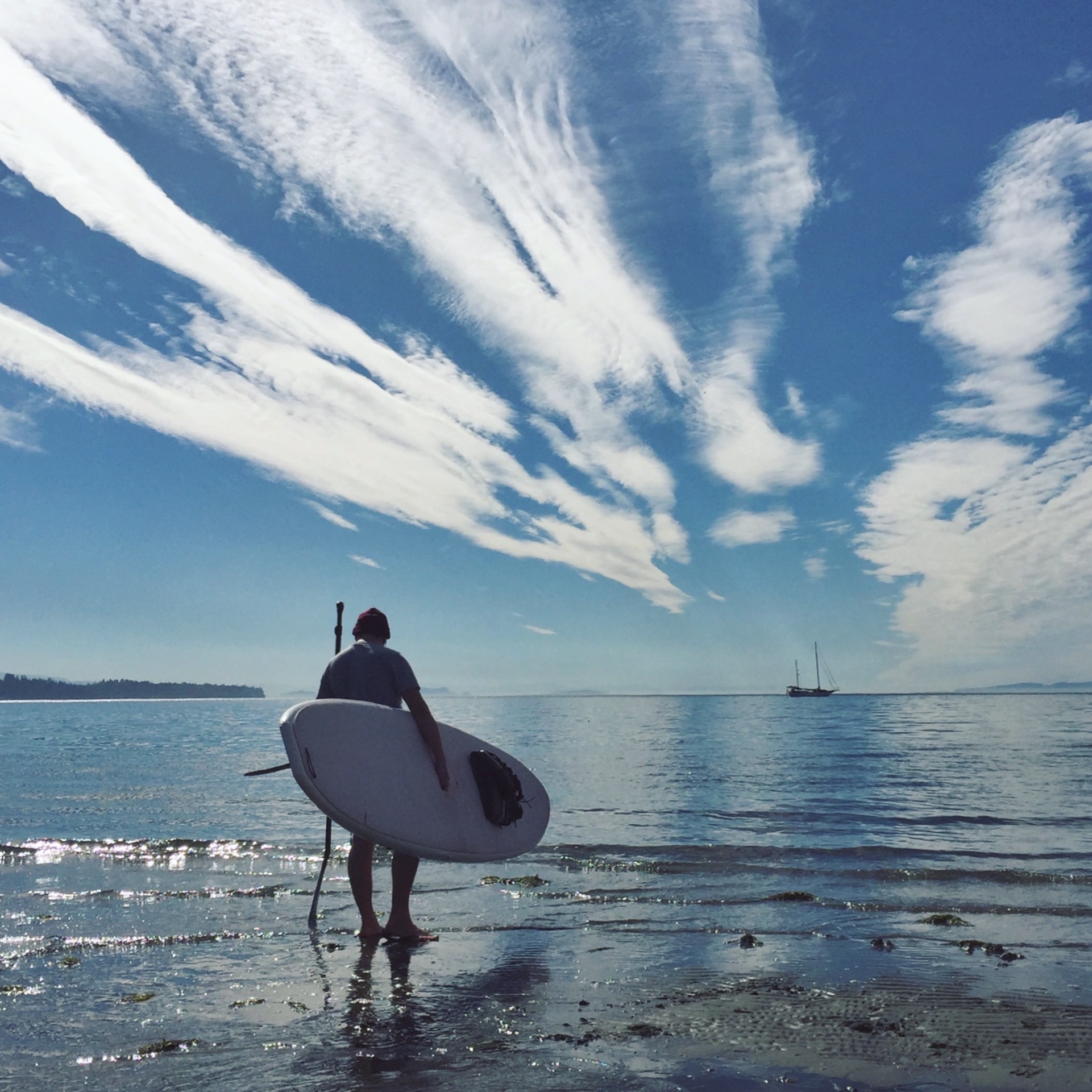 Josh holding his paddle board on the beach looking out into the ocean.